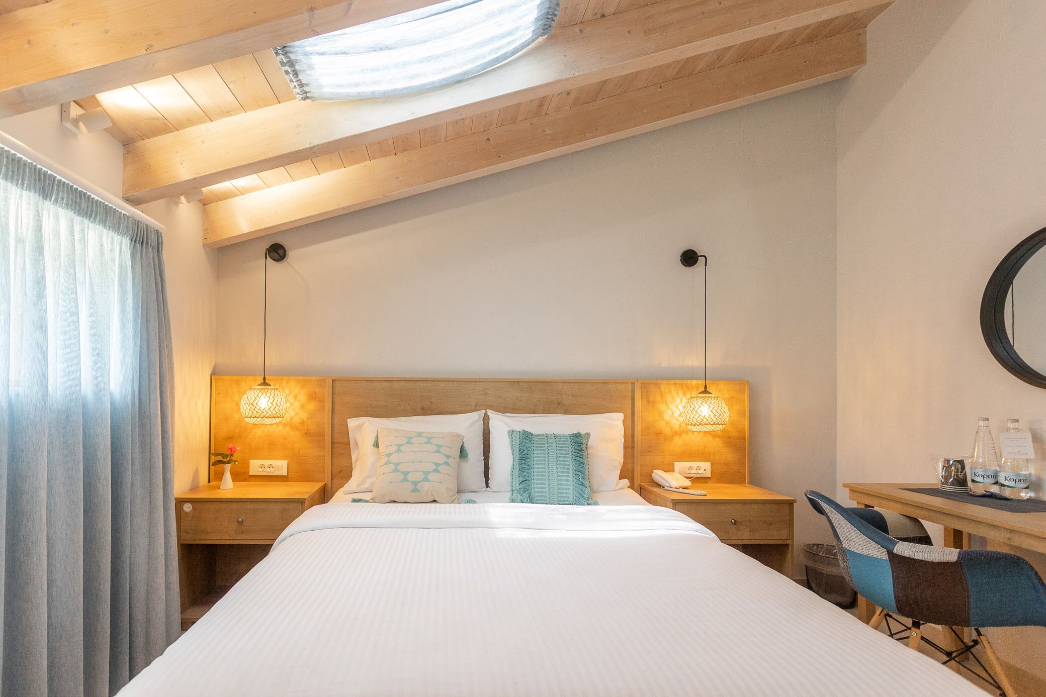 Ein Hotelzimmer mit einem großen Bett, einem Holz-Kopfteil, zwei Nachttischlampen, einem Schreibtisch mit Stuhl und einem runden Spiegel an der Wand.