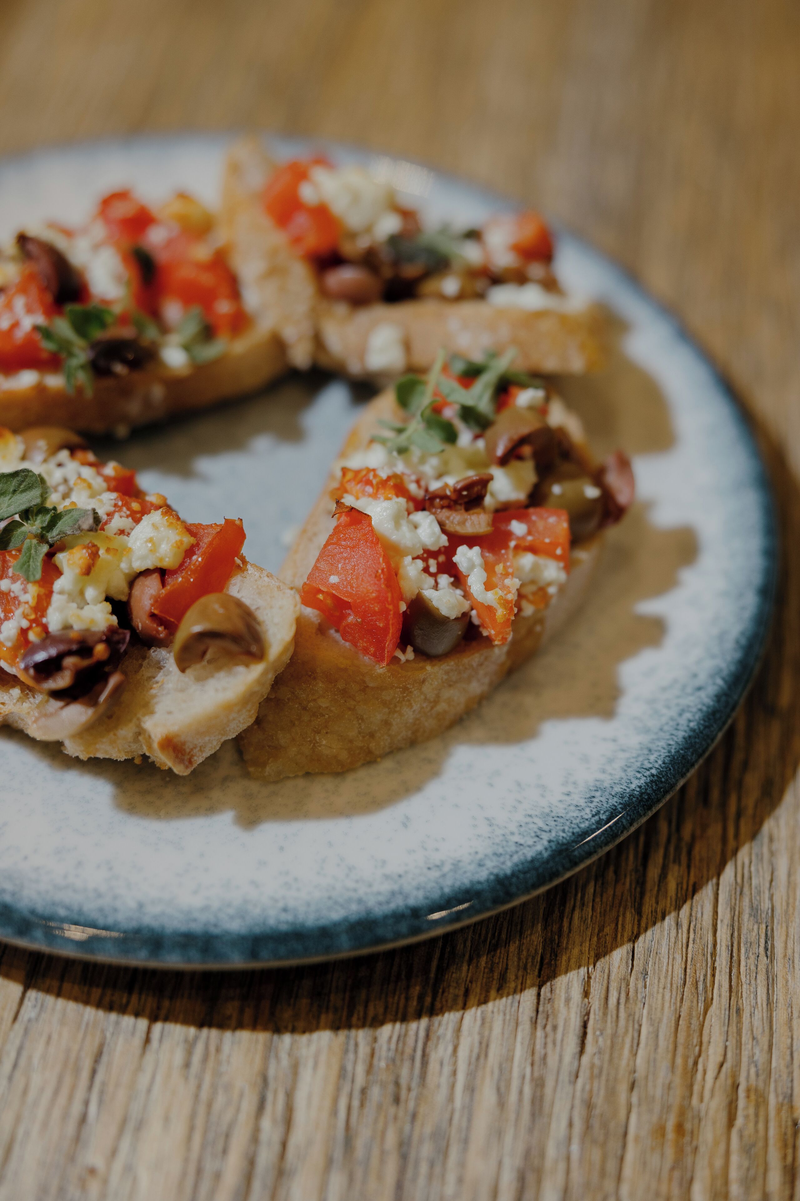 Un piatto con diverse bruschette condite con pomodori, formaggio e erbe aromatiche.