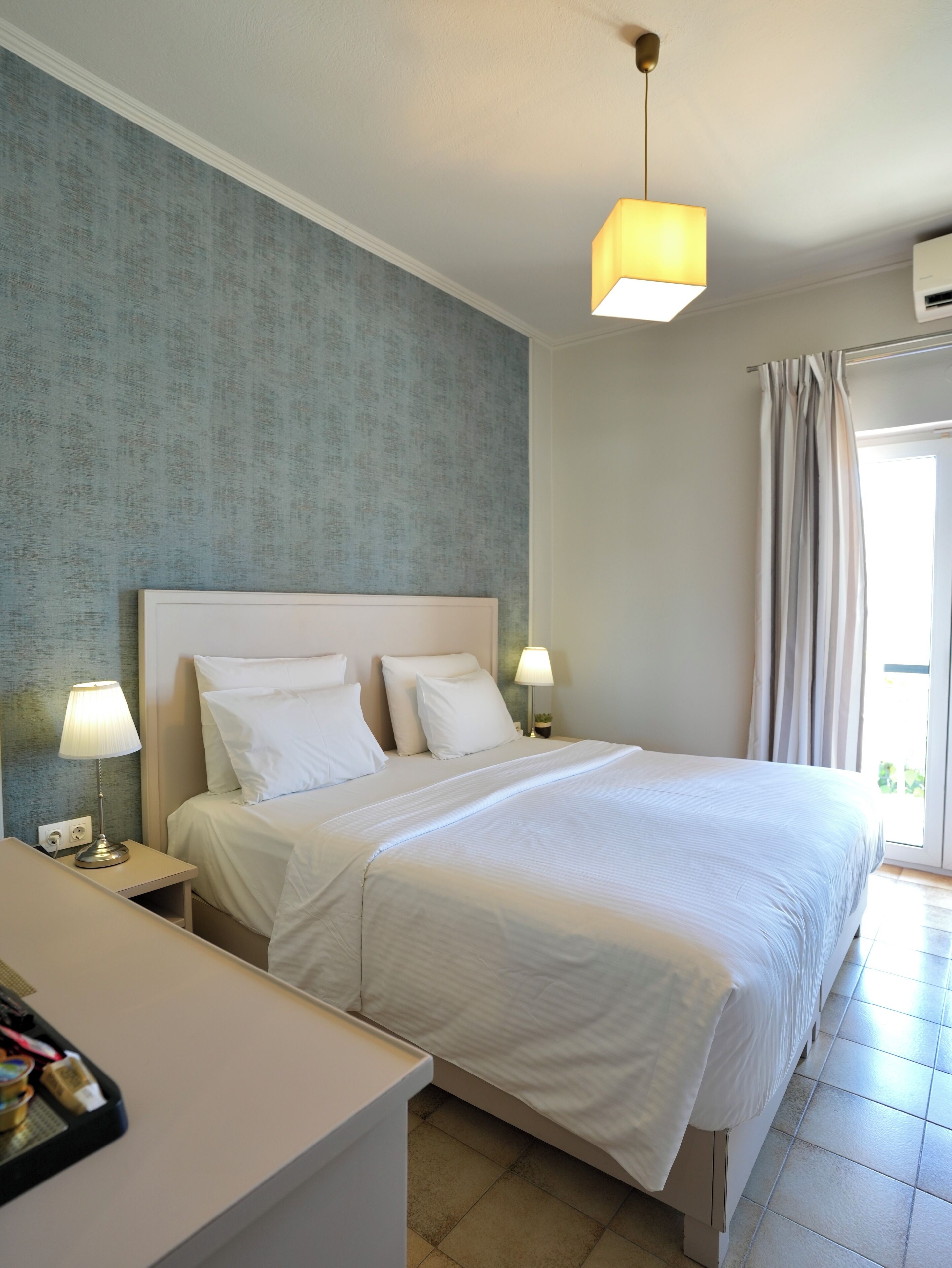 A neatly made bed with white linens, two bedside lamps, and a wall-mounted air conditioner.