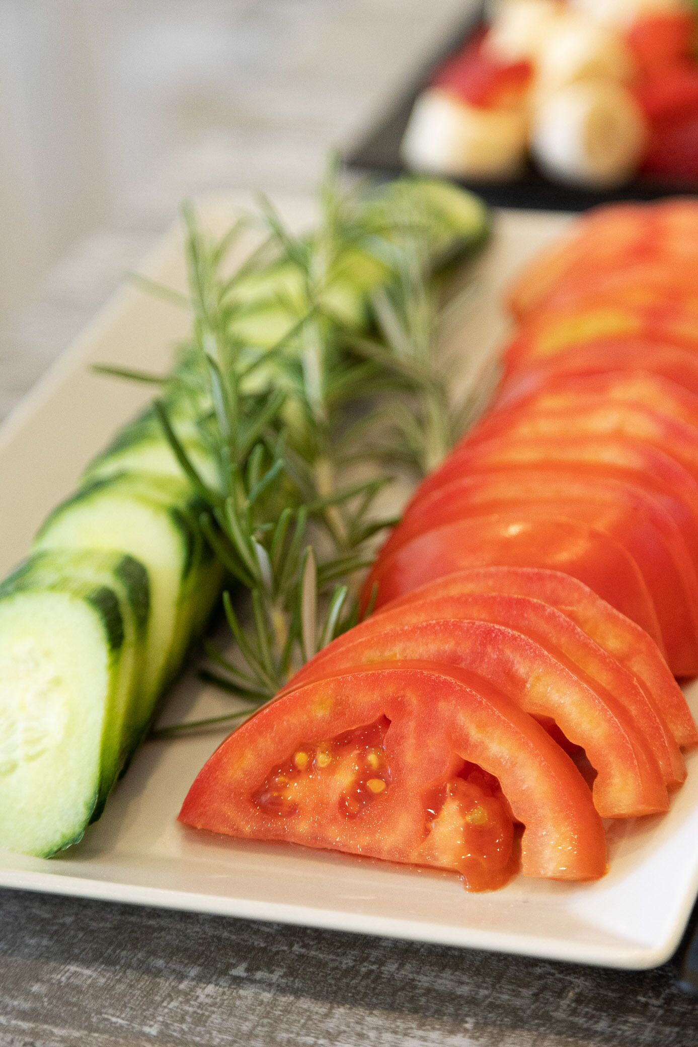 A plate with sliced tomatoes, cucumber, and rosemary.