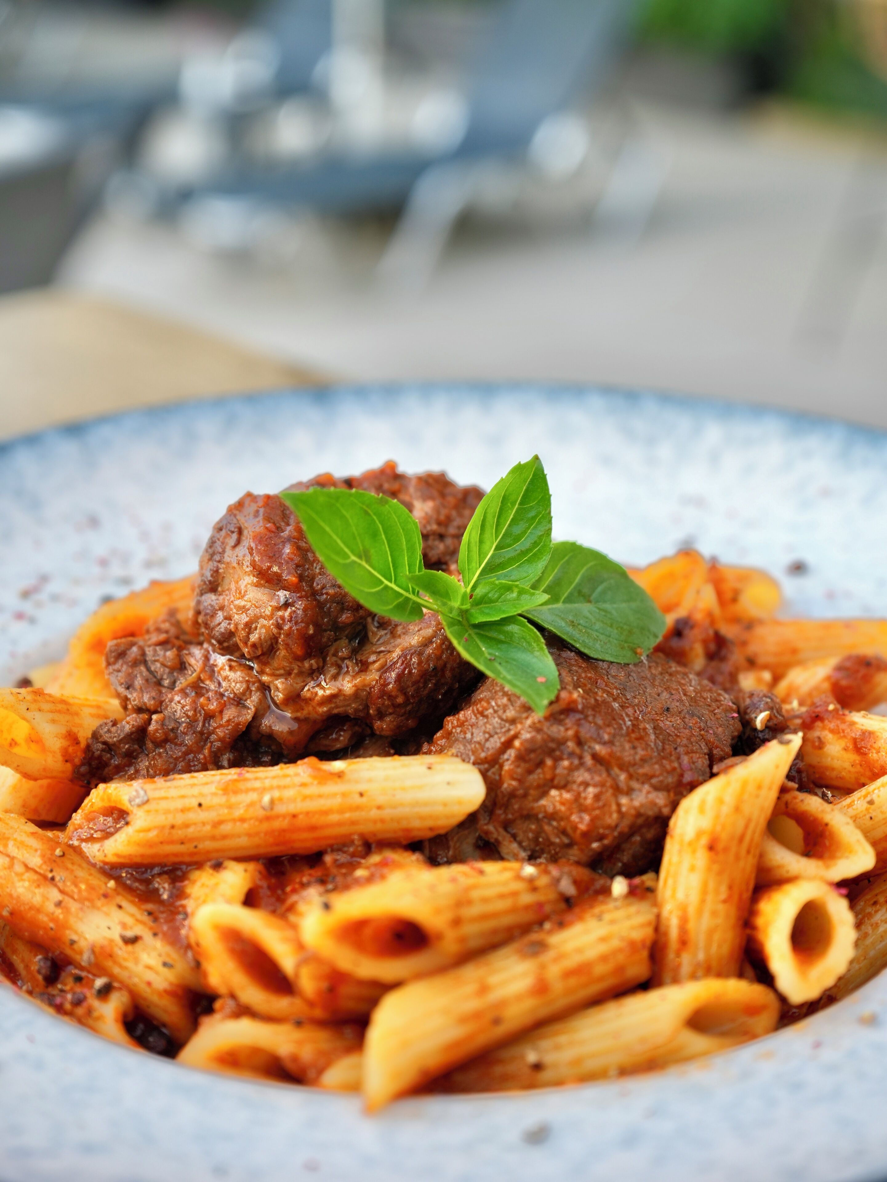 A plate of pasta with meat and a basil leaf garnish.