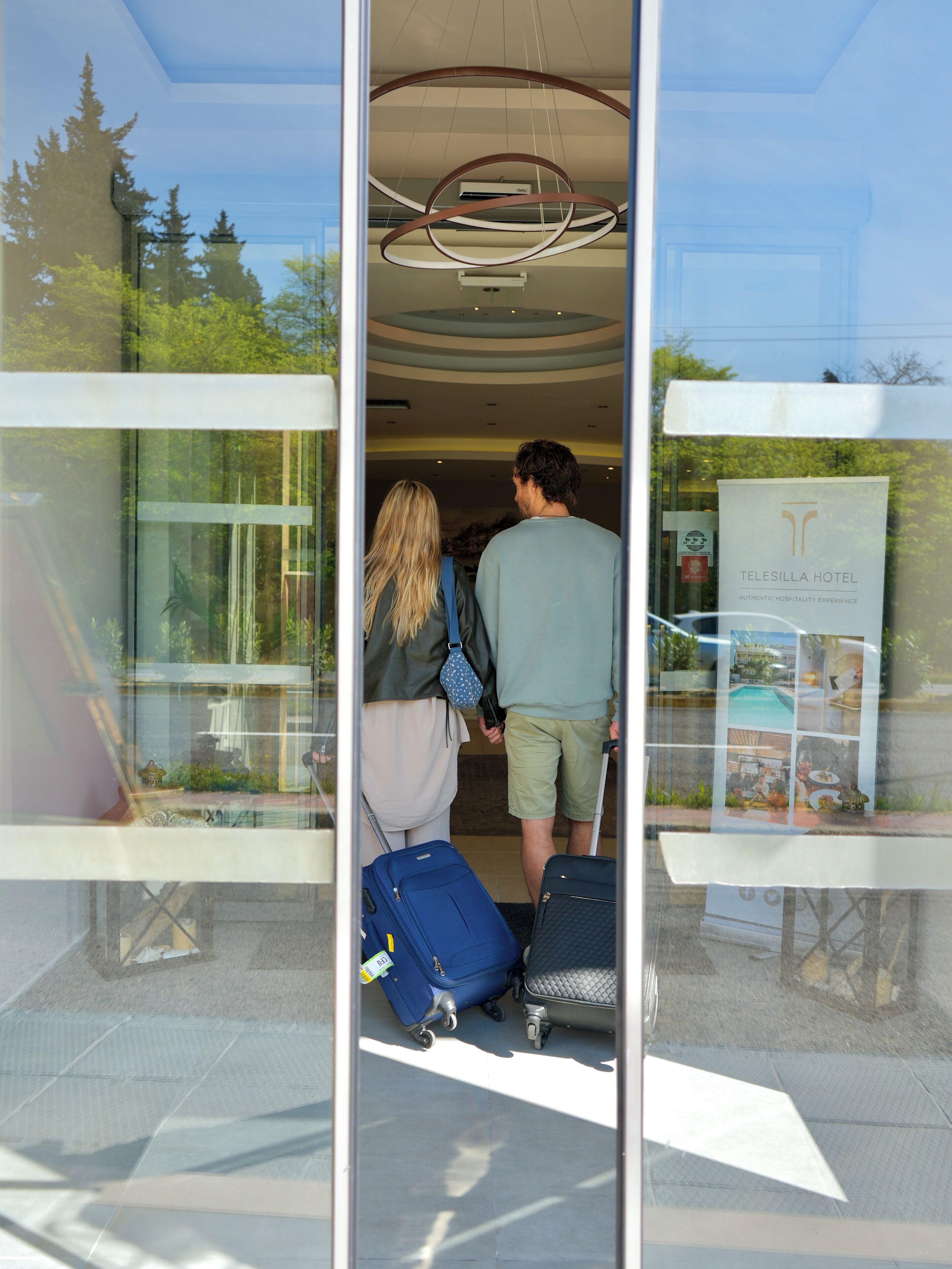 A hotel entrance with glass doors, a sign for the hotel, and a view of the surrounding greenery.