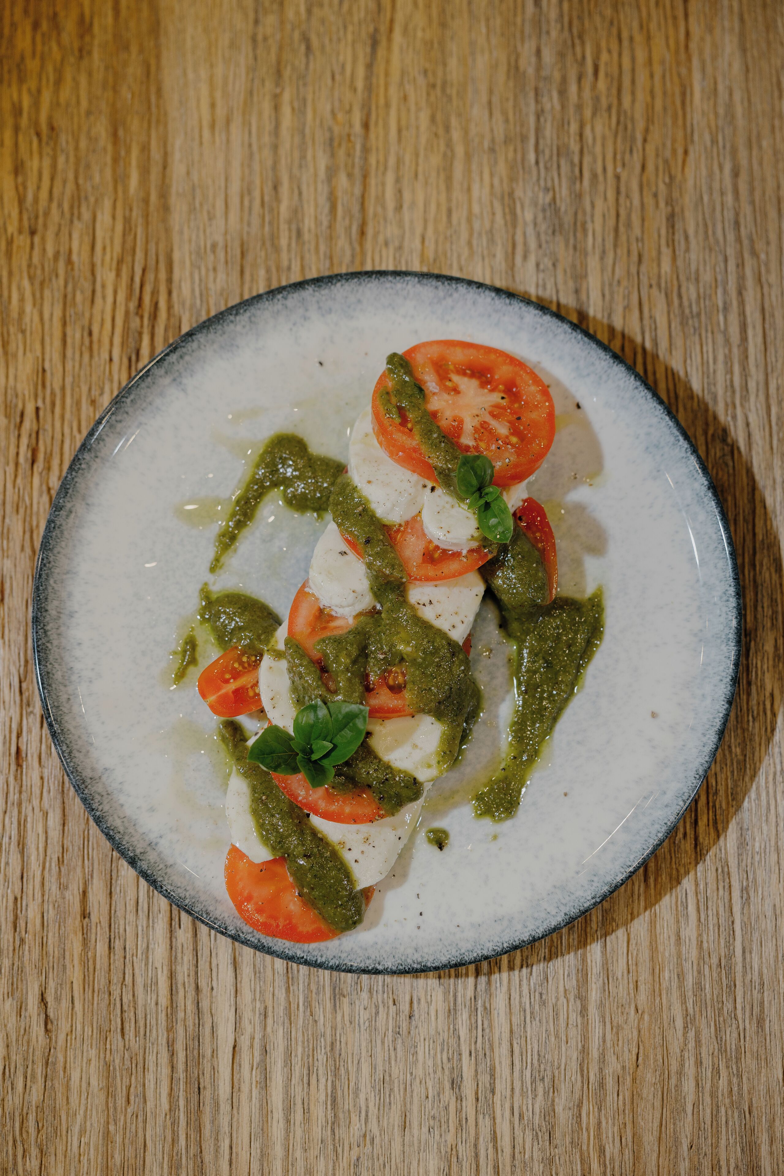 A plate of Caprese salad with tomatoes, mozzarella, and basil on a wooden table.
