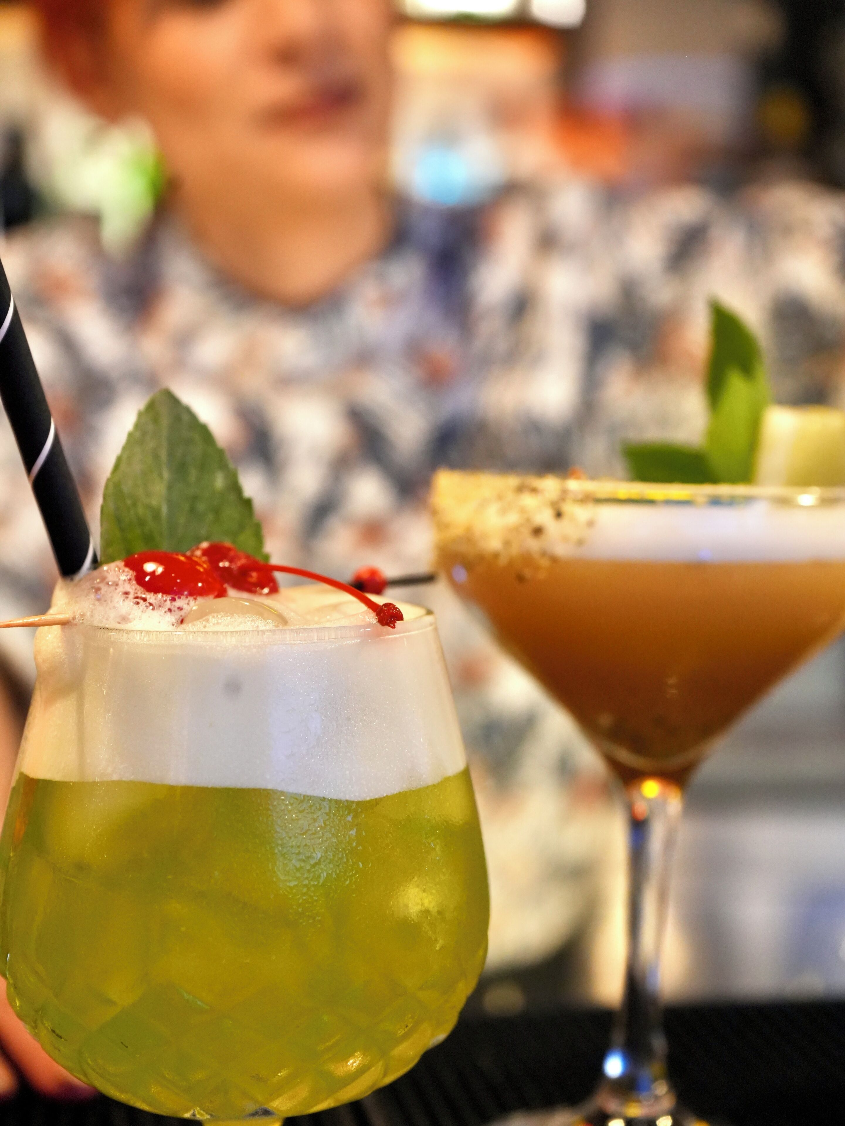 Two cocktails with garnishes, one with a straw and mint, and another with a rim.