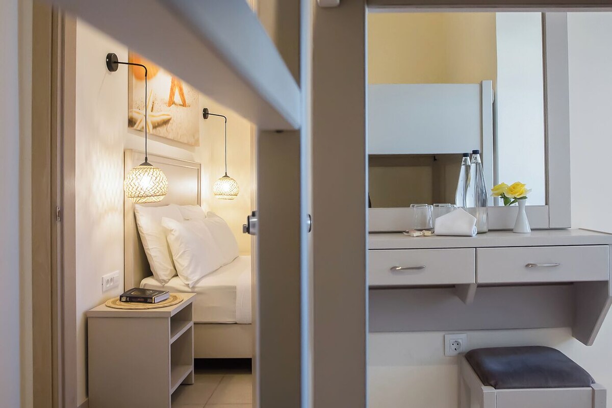 Et moderne hotelværelse med seng, sengebord, lampe og et skrivebord med stol.