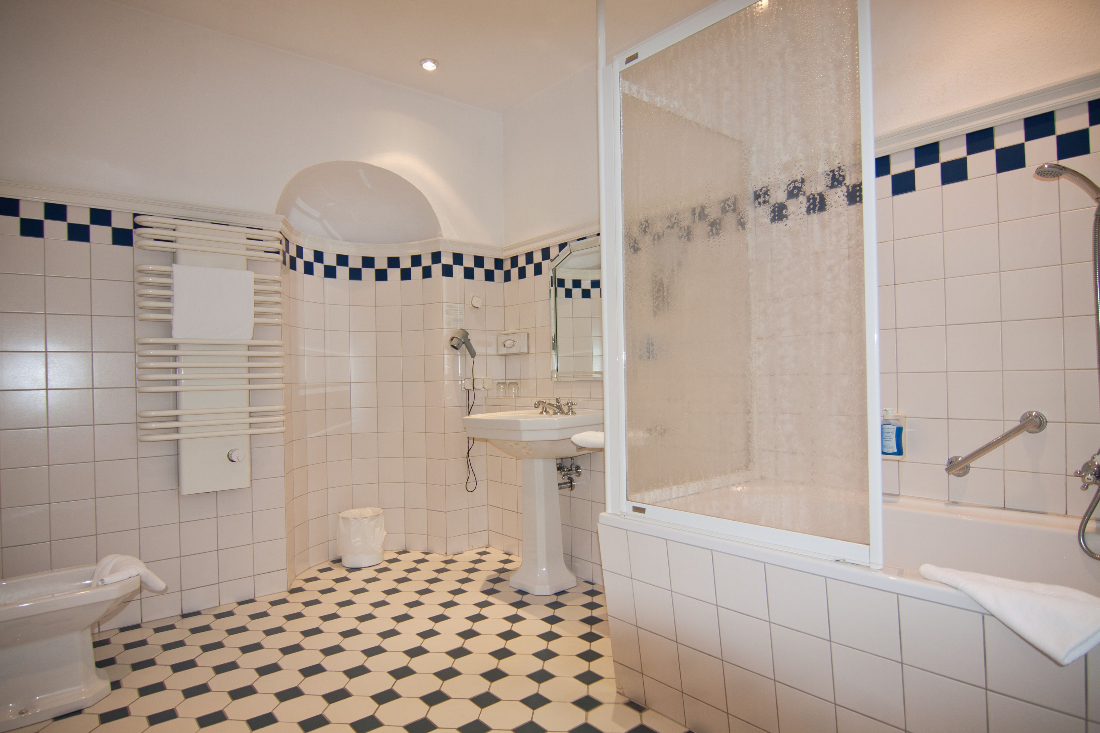 A bathroom with a checkered floor, a pedestal sink, a shower with a glass door, and a towel rack.
