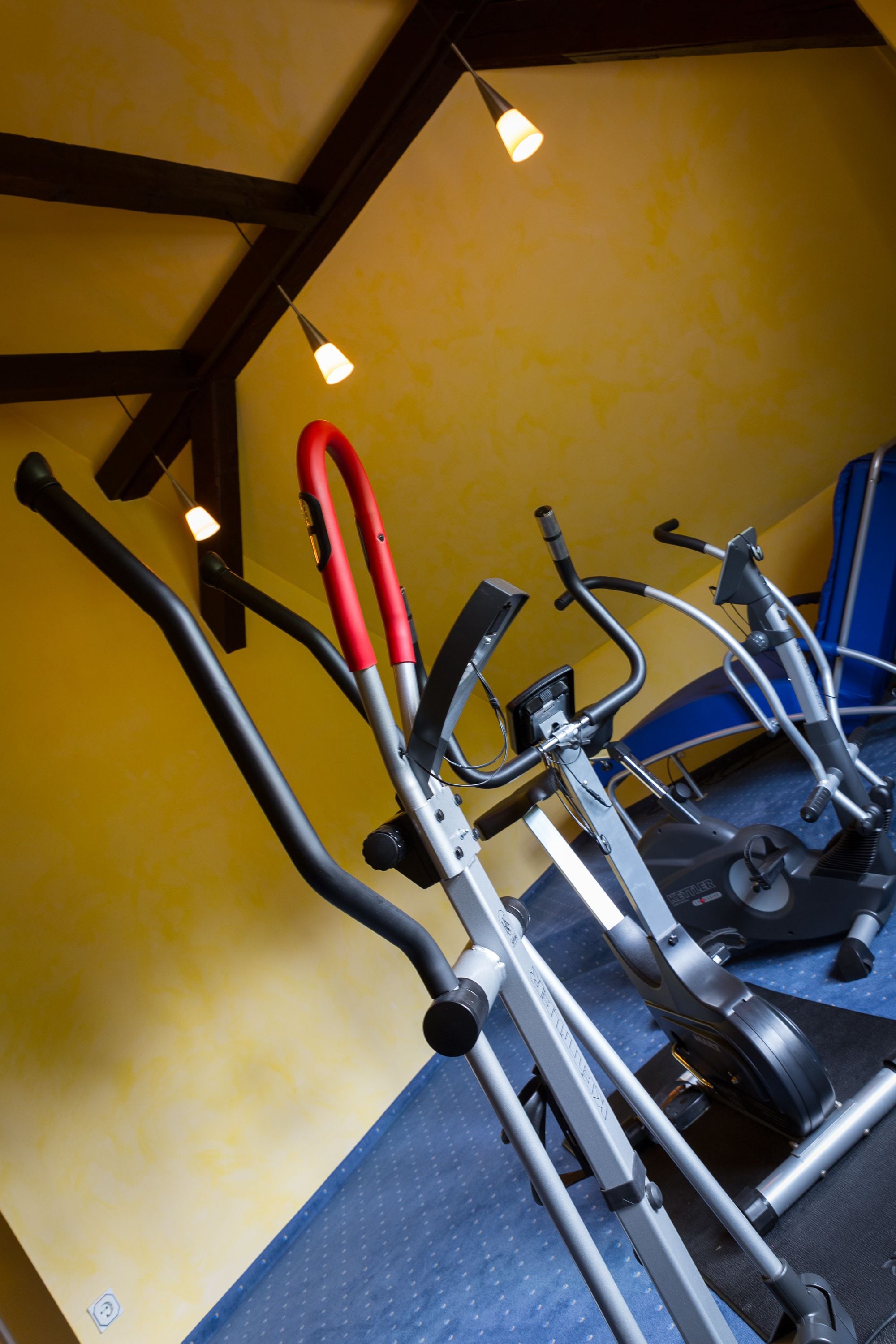 Varias bicicletas estáticas en una habitación con paredes amarillas y un tapete azul en el suelo.