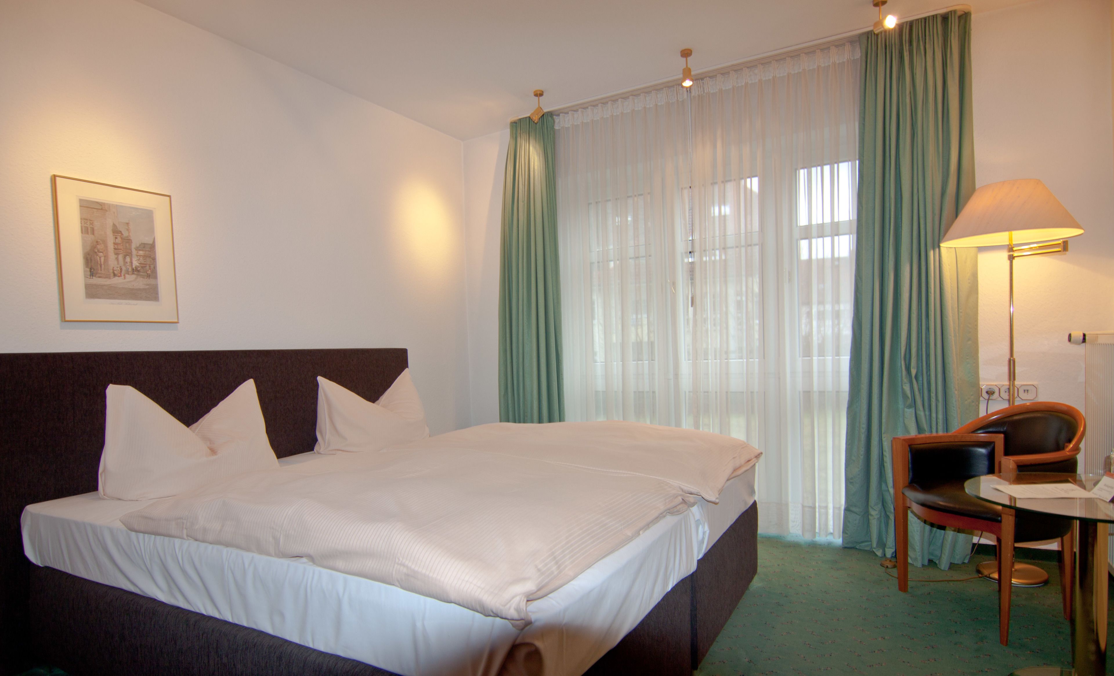 A hotel room with a large bed, a chair, a desk, and a lamp.