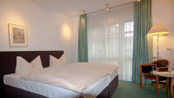 A hotel room with a large bed, a chair, a desk, and a lamp.