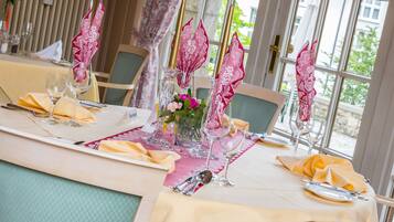 Una mesa de comedor dispuesta con servilletas rosas, cristalería transparente y un jarrón con flores.