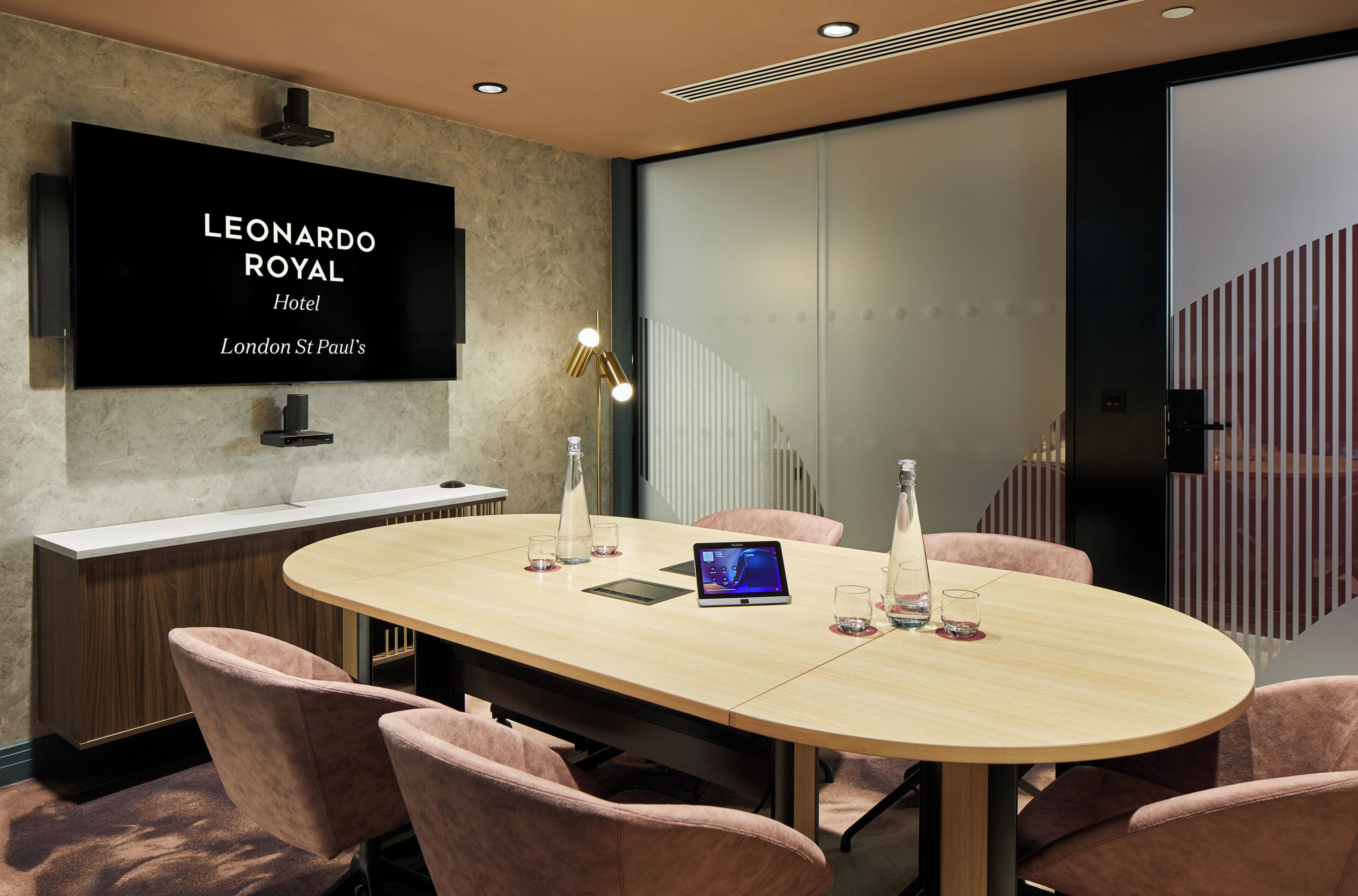 A conference room with a long table, chairs, a flat-screen TV, and a bottle of water.