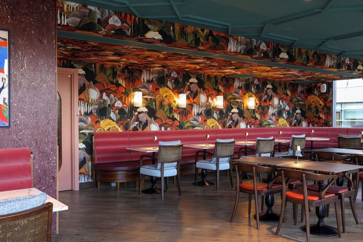 A restaurant interior with red booths, wooden tables, wicker chairs, and a colorful mural on the ceiling.