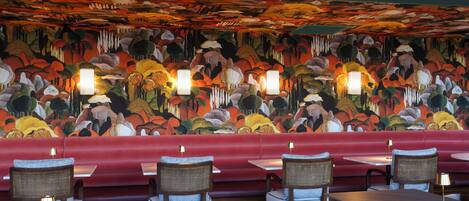A restaurant interior with a vibrant mural, red seating, and tables with lamps.