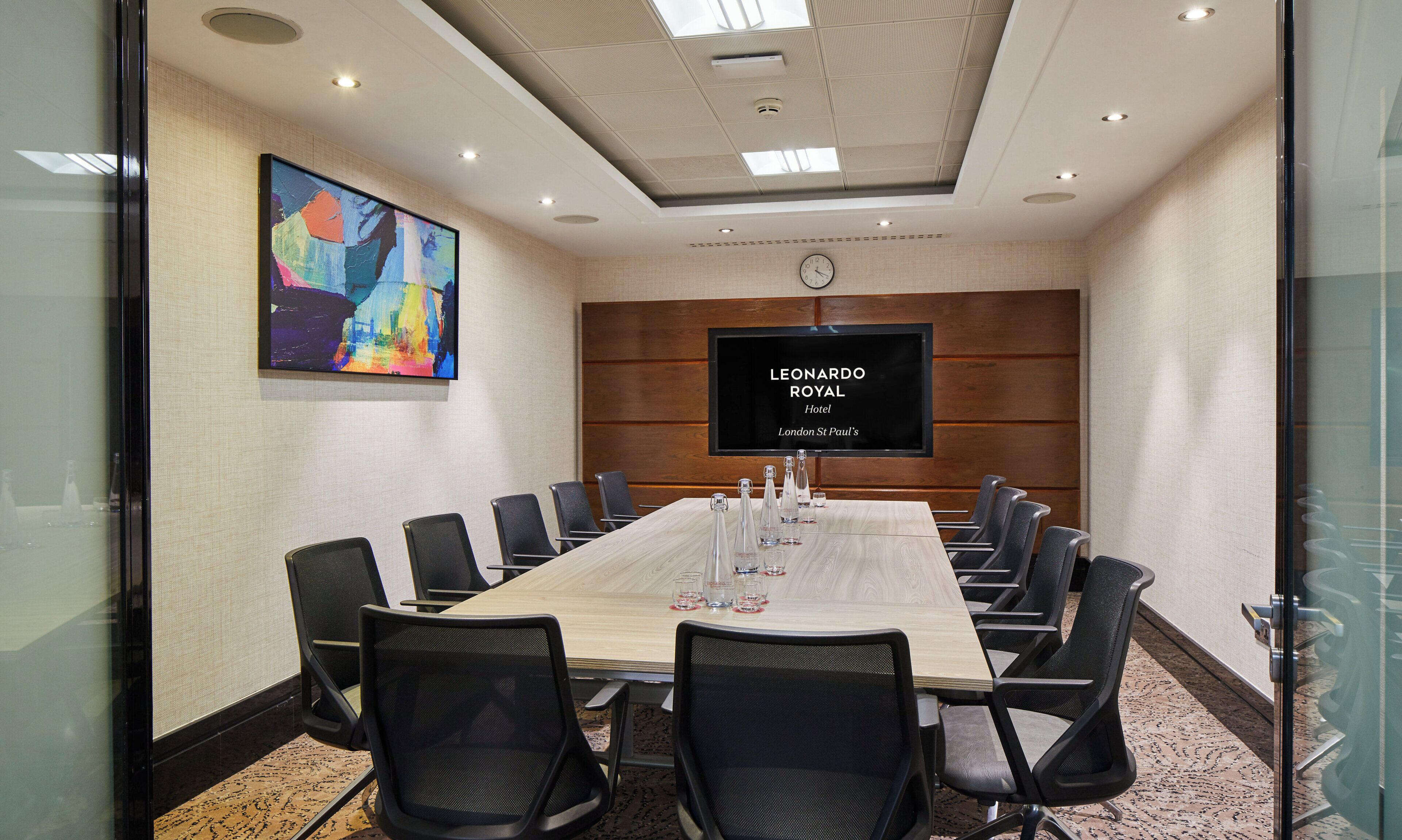 Une salle de conférence avec une longue table, des chaises, un téléviseur à écran plat et une horloge au mur.