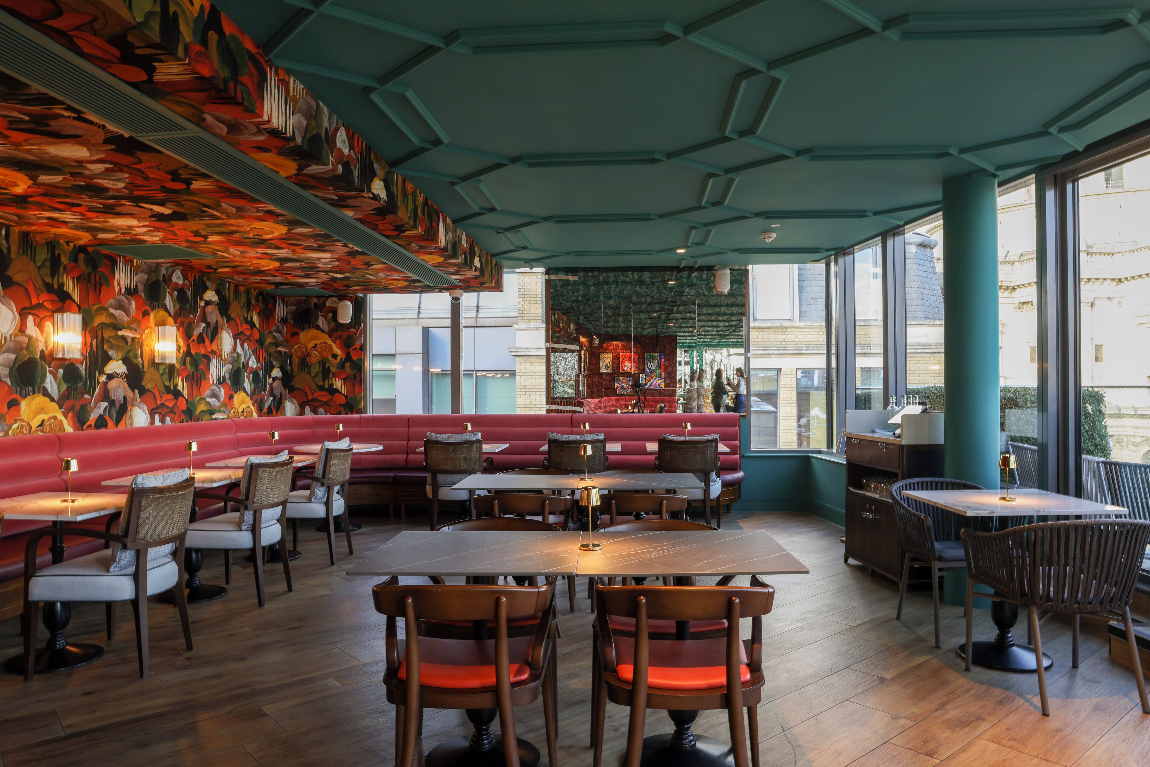 A restaurant interior with wooden tables and chairs, a red bench seating area, and a mural on the ceiling.