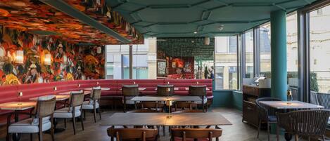 A restaurant interior with wooden tables and chairs, a red bench seating area, and a mural on the ceiling.