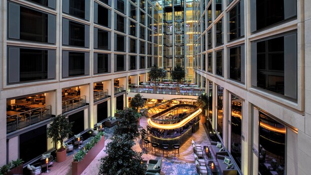 Un atrium à plusieurs niveaux comprenant un bar central, des espaces de détente et de la verdure.
