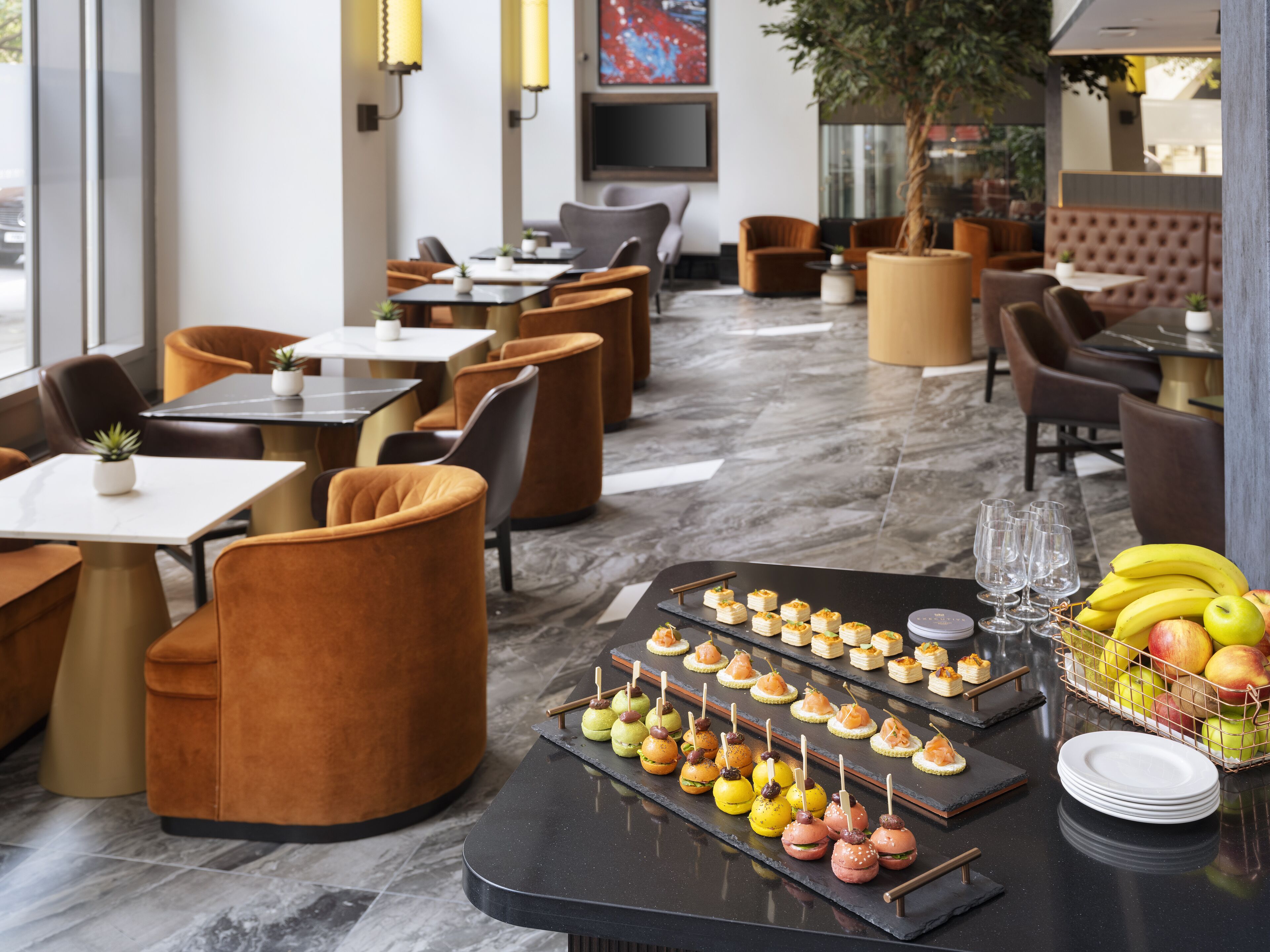A restaurant with a modern interior, featuring round tables, cushioned chairs, and a marble floor.