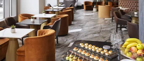 A restaurant with a modern interior, featuring round tables, cushioned chairs, and a marble floor.