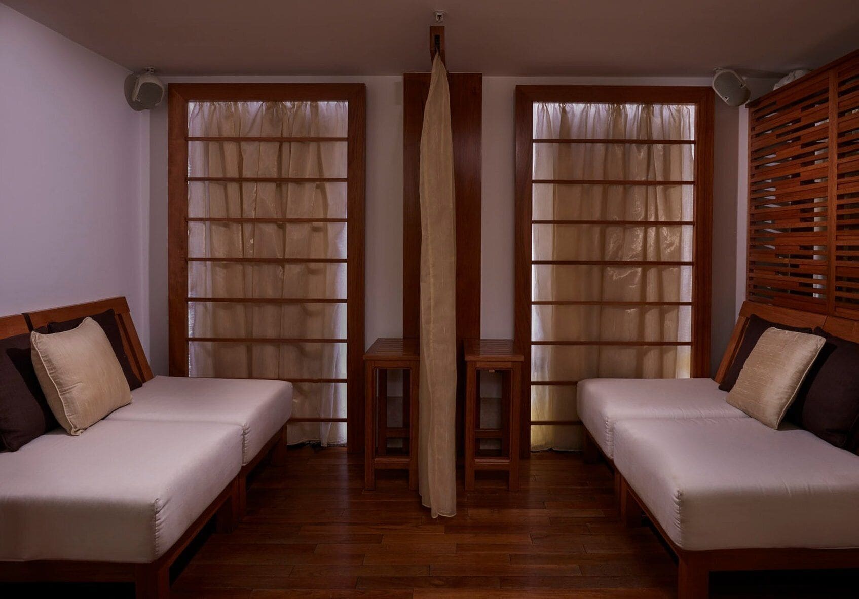 Habitación con dos camas, piso de madera y un separador central con cortina.