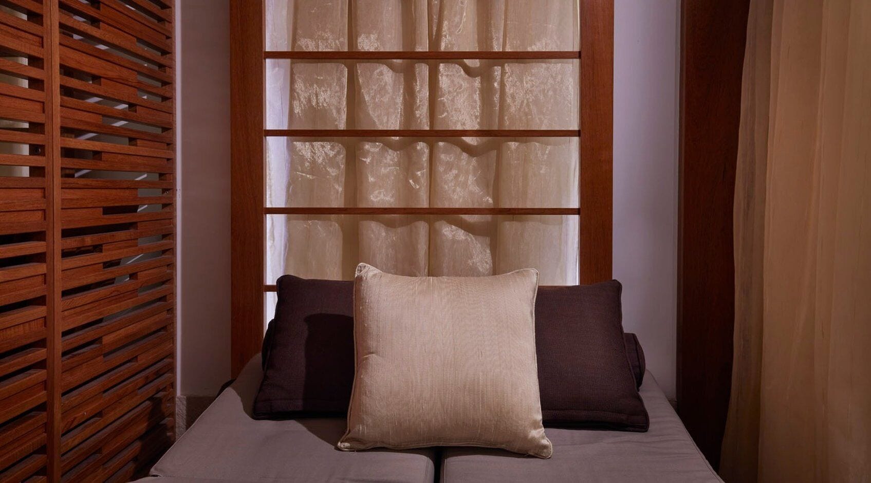 A bedroom with a bed, two pillows, a wooden slat headboard, and sheer curtains.