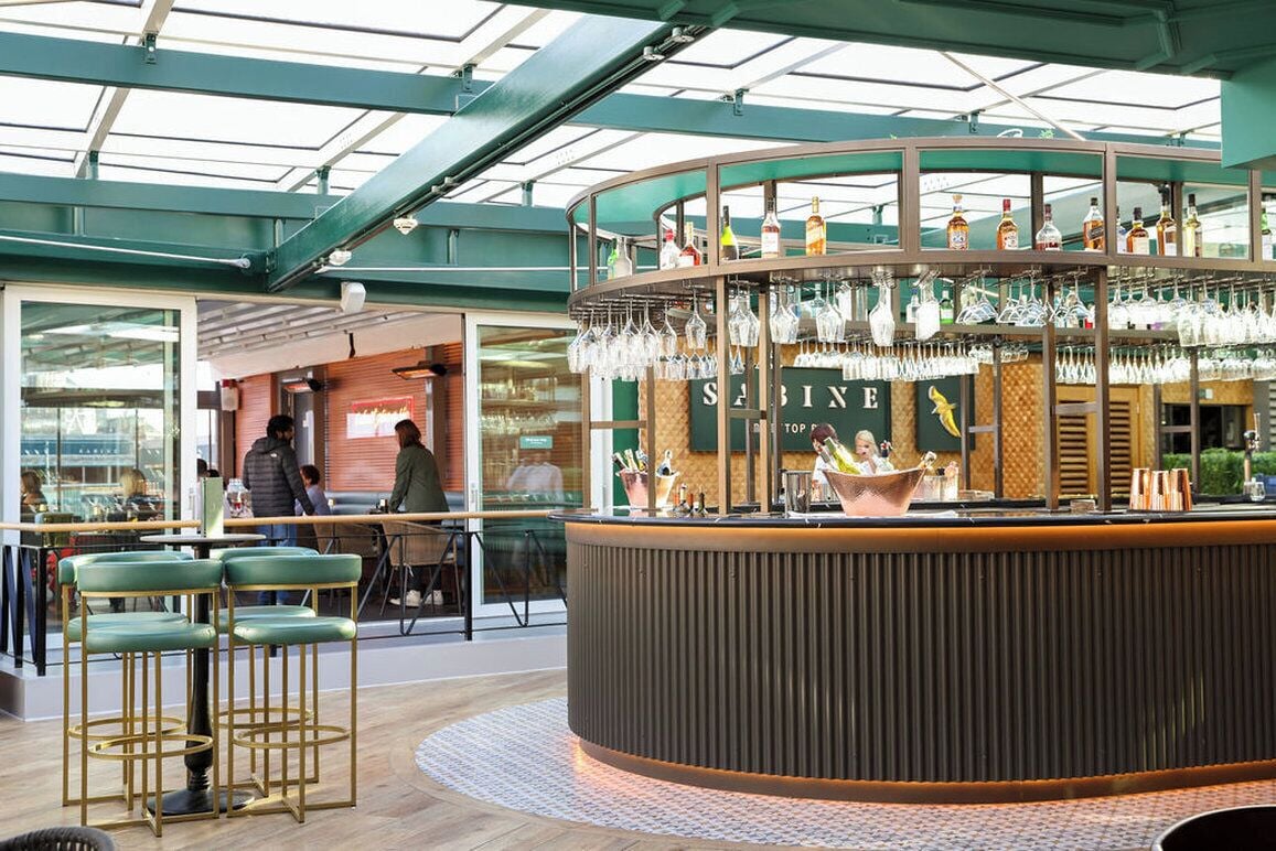 A bar area with a curved counter, hanging glasses, and stools.