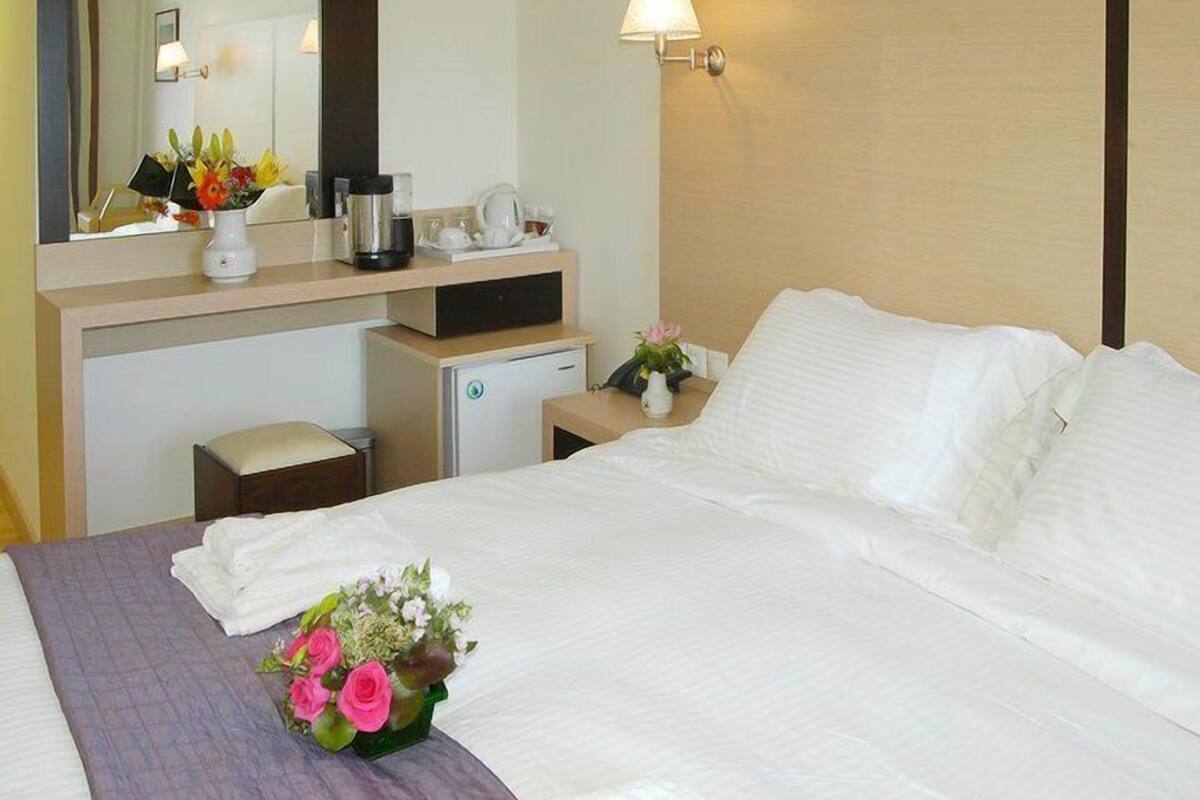 Habitación de hotel con cama, escritorio, cafetera, refrigerador pequeño y espejo.