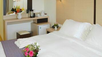 A hotel room with a bed, a desk with a coffee maker, a mini-fridge, and a mirror.