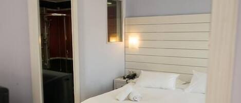 A hotel room with a bed, a bedside table, a nightstand, and a mirror.