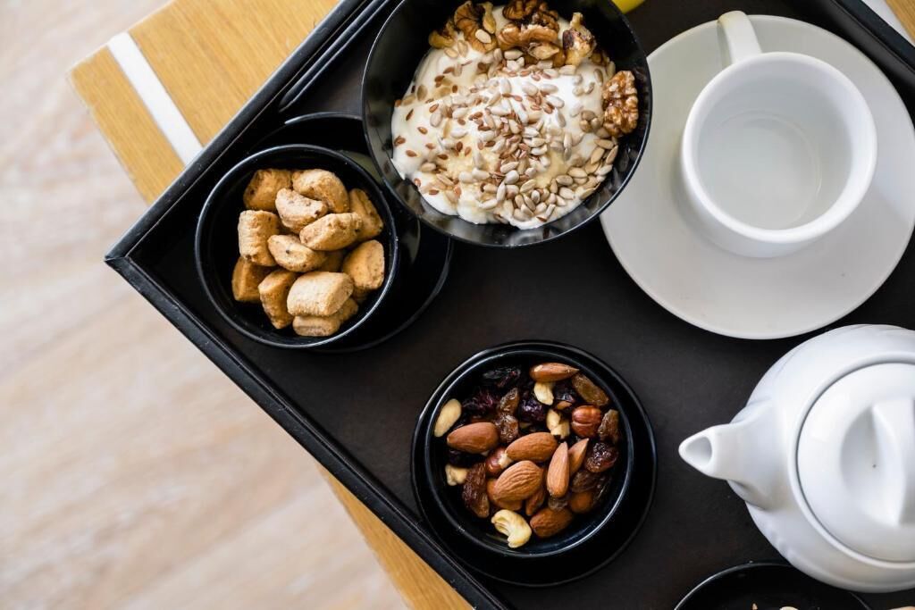 A tray with bowls of nuts, dried fruits, and cookies, a cup, and a teapot.