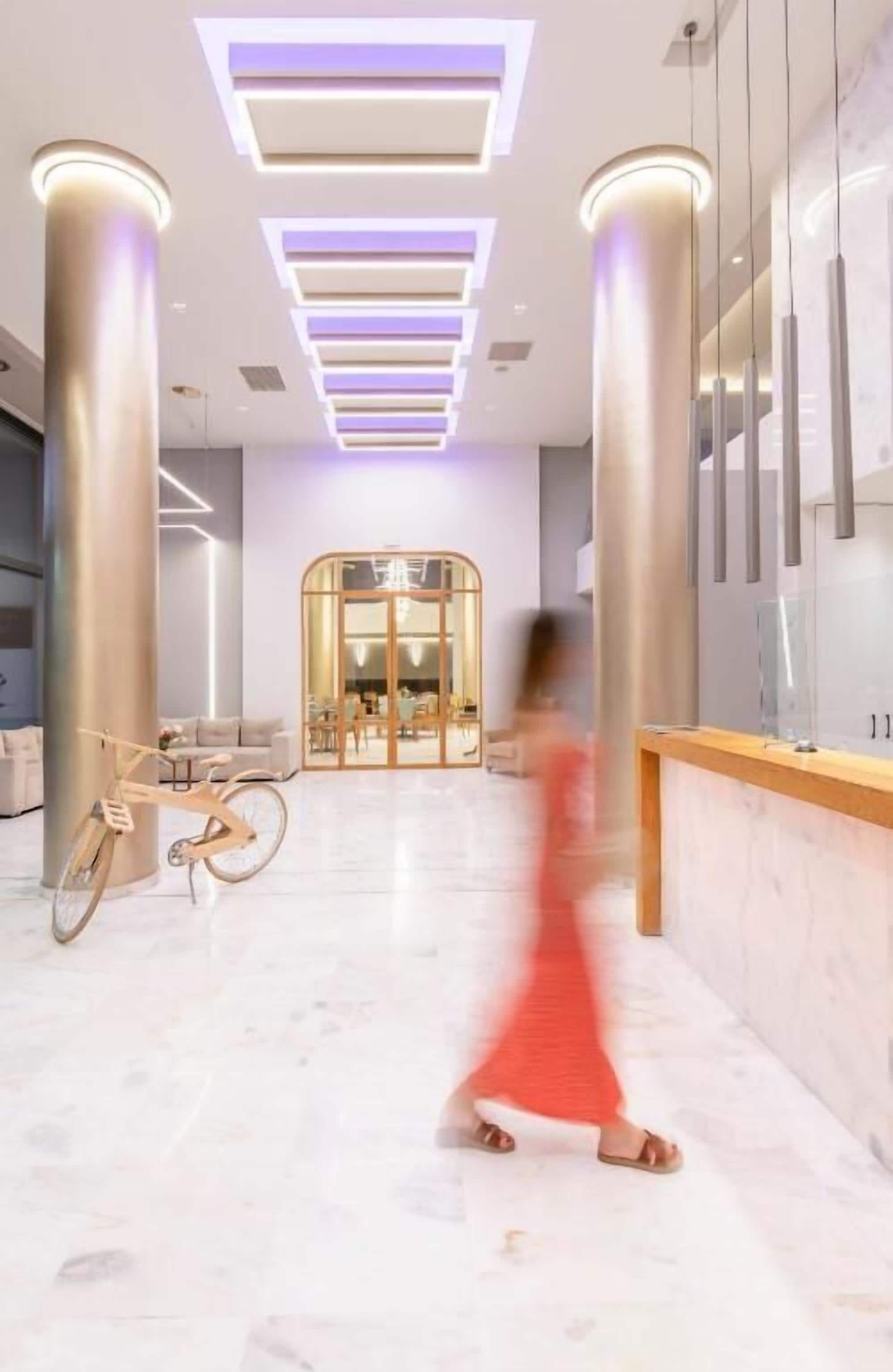 A modern hotel lobby with a central seating area, a reception desk, and a bicycle.