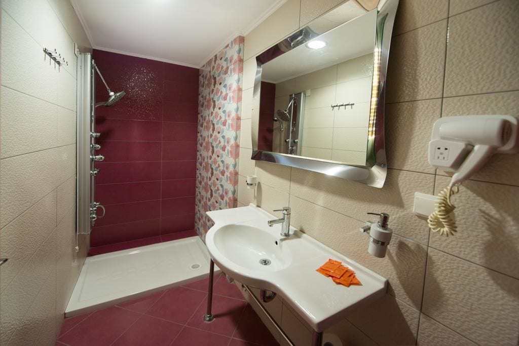 A bathroom with a shower, a sink, a mirror, and a hairdryer on the wall.