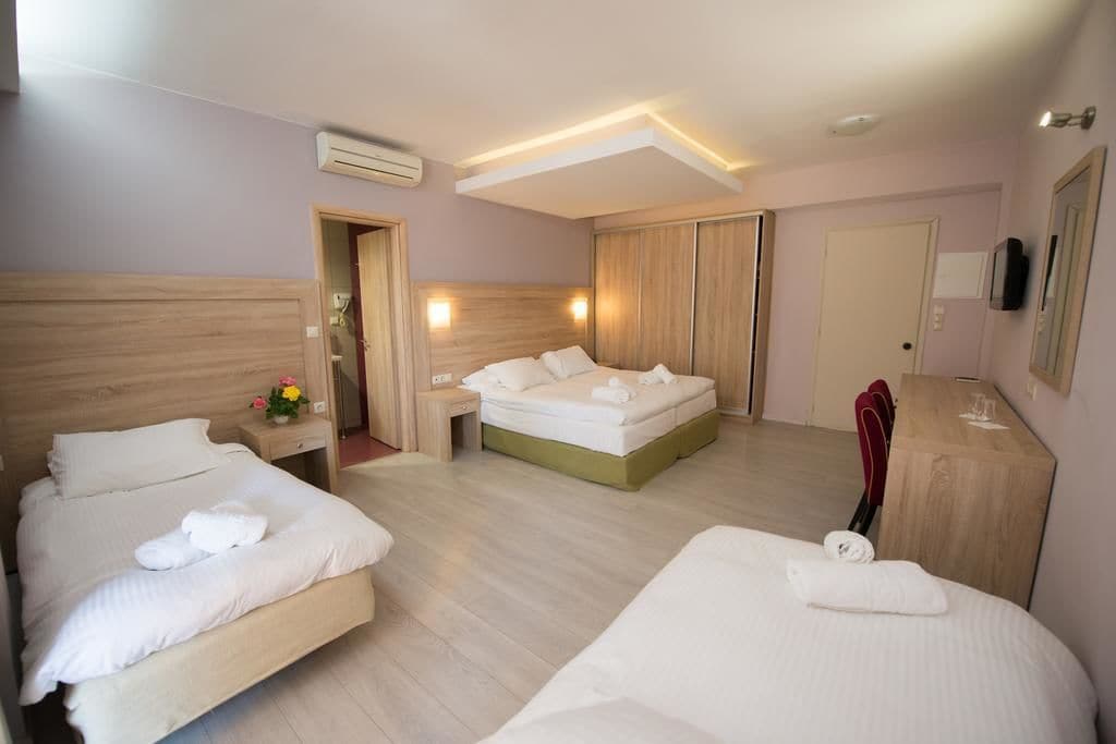 Une chambre d’hôtel avec deux lits, une tête de lit en bois, une table de chevet avec une lampe, un miroir et une armoire.