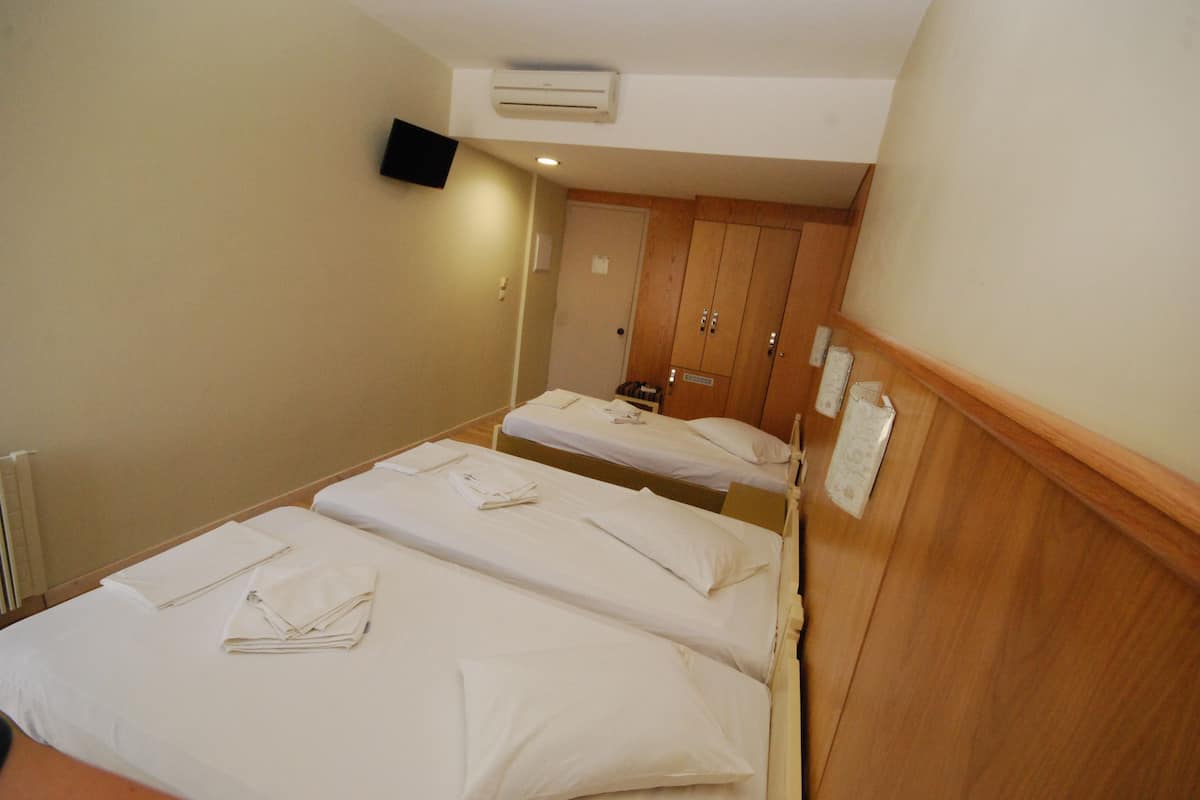 Habitación de hotel con dos camas individuales, un armario de madera, un televisor de pantalla plana montado en la pared y un equipo de aire acondicionado.