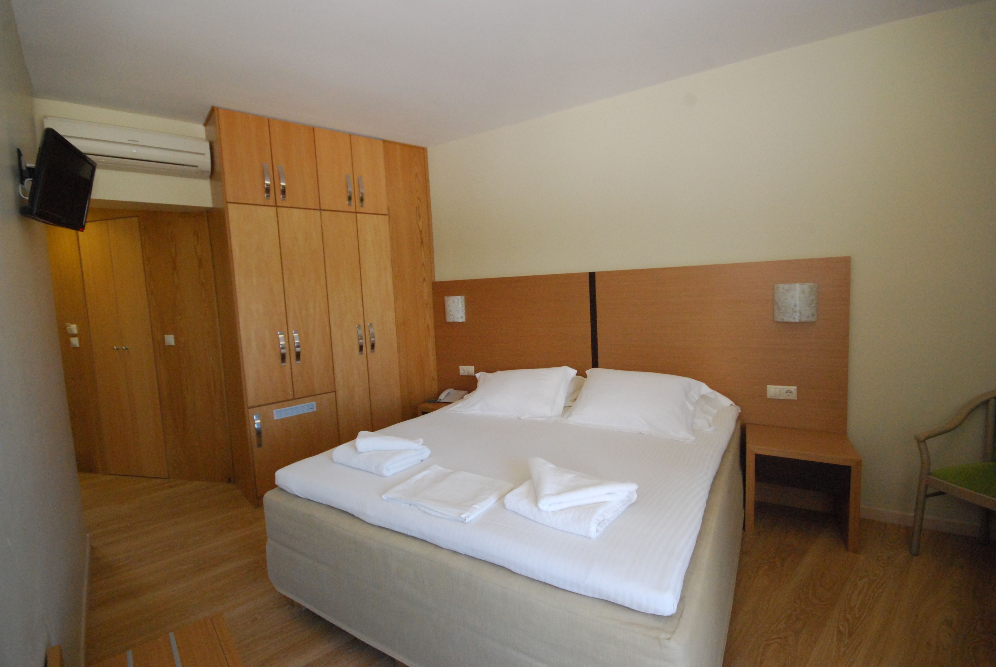 A hotel room with a large bed, wooden wardrobe, bedside table, and a television mounted on the wall.