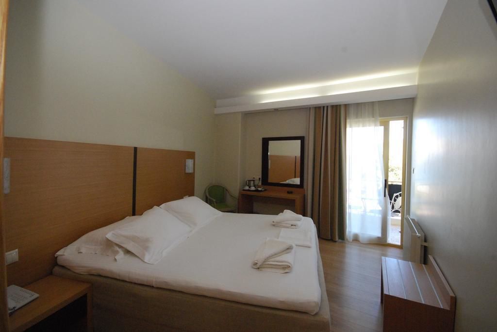 Une chambre d’hôtel avec un grand lit, une tête de lit en bois, un bureau avec une chaise, un miroir et une vue sur l’extérieur par une fenêtre.