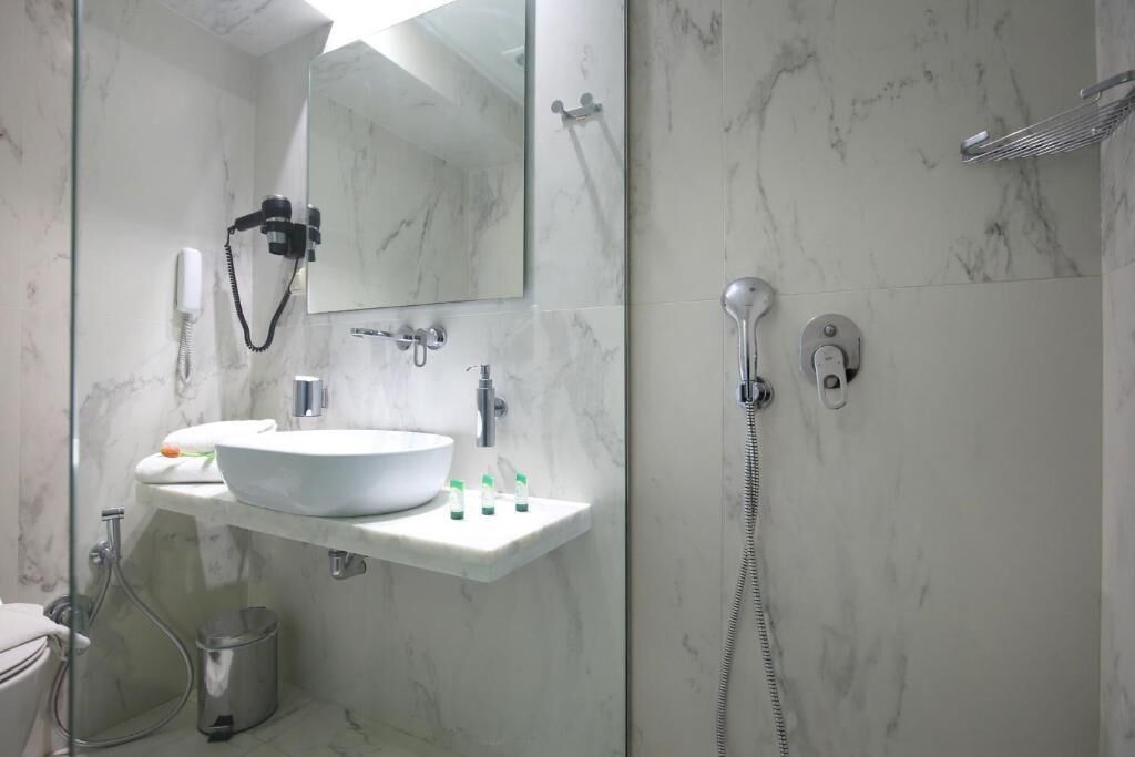 Een moderne badkamer met een marmeren wastafel, een spiegel, een handdouche en een toilet aan de muur bevestigd.