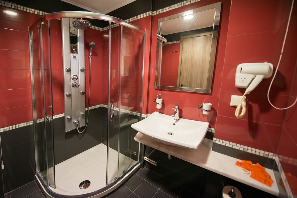 A modern bathroom with a glass-enclosed shower, a white sink, and a red-tiled wall.