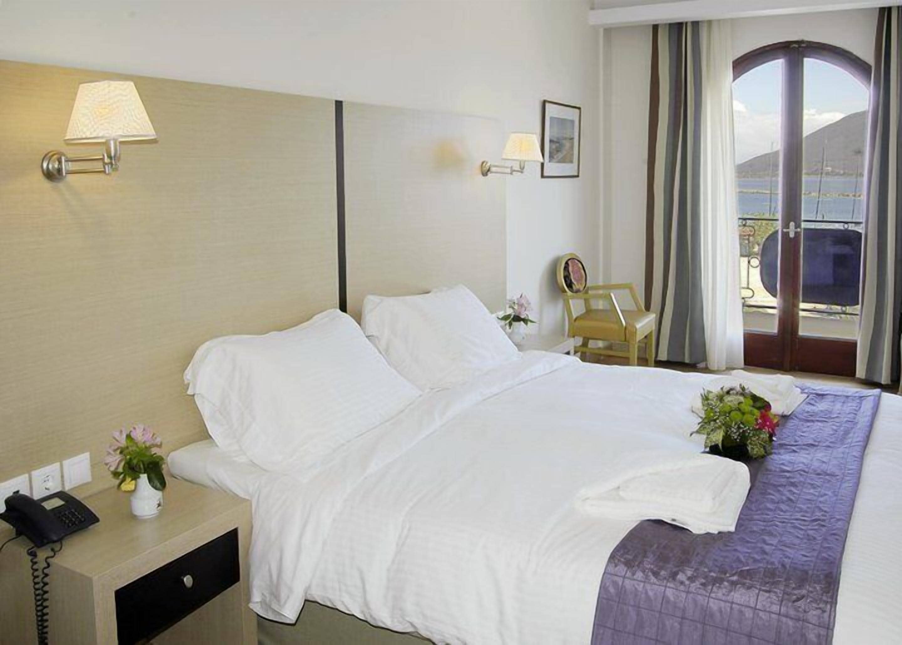 A hotel room with a bed, bedside table, lamp, chair, and a view of the outdoors.