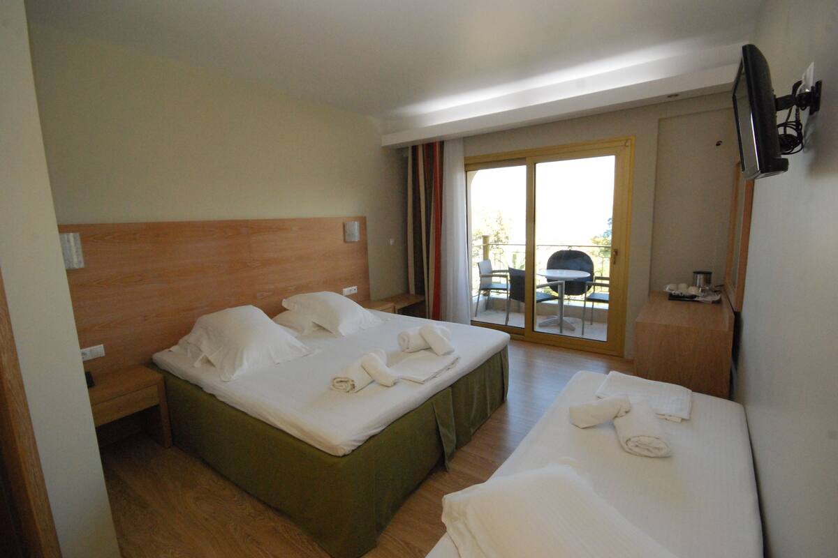 Habitación de hotel con dos camas, un cabecero de madera, un escritorio pequeño y un ventanal corredero que da a un área exterior.