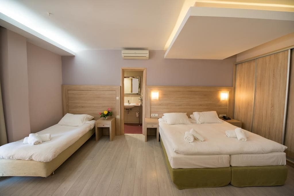 A hotel room with two single beds, a wooden headboard, a nightstand with a lamp, and a mirror.