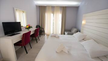 Habitación de hotel con cama, escritorio con televisor, una silla y ventana con cortinas.