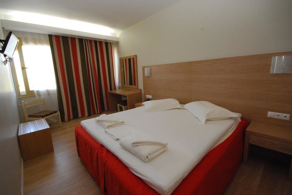 A hotel room with a large bed, a desk, a chair, and a window with striped curtains.