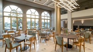 Un vaste espace dédié à la salle à manger, avec de nombreuses tables et chaises, de grandes fenêtres et un lustre moderne.