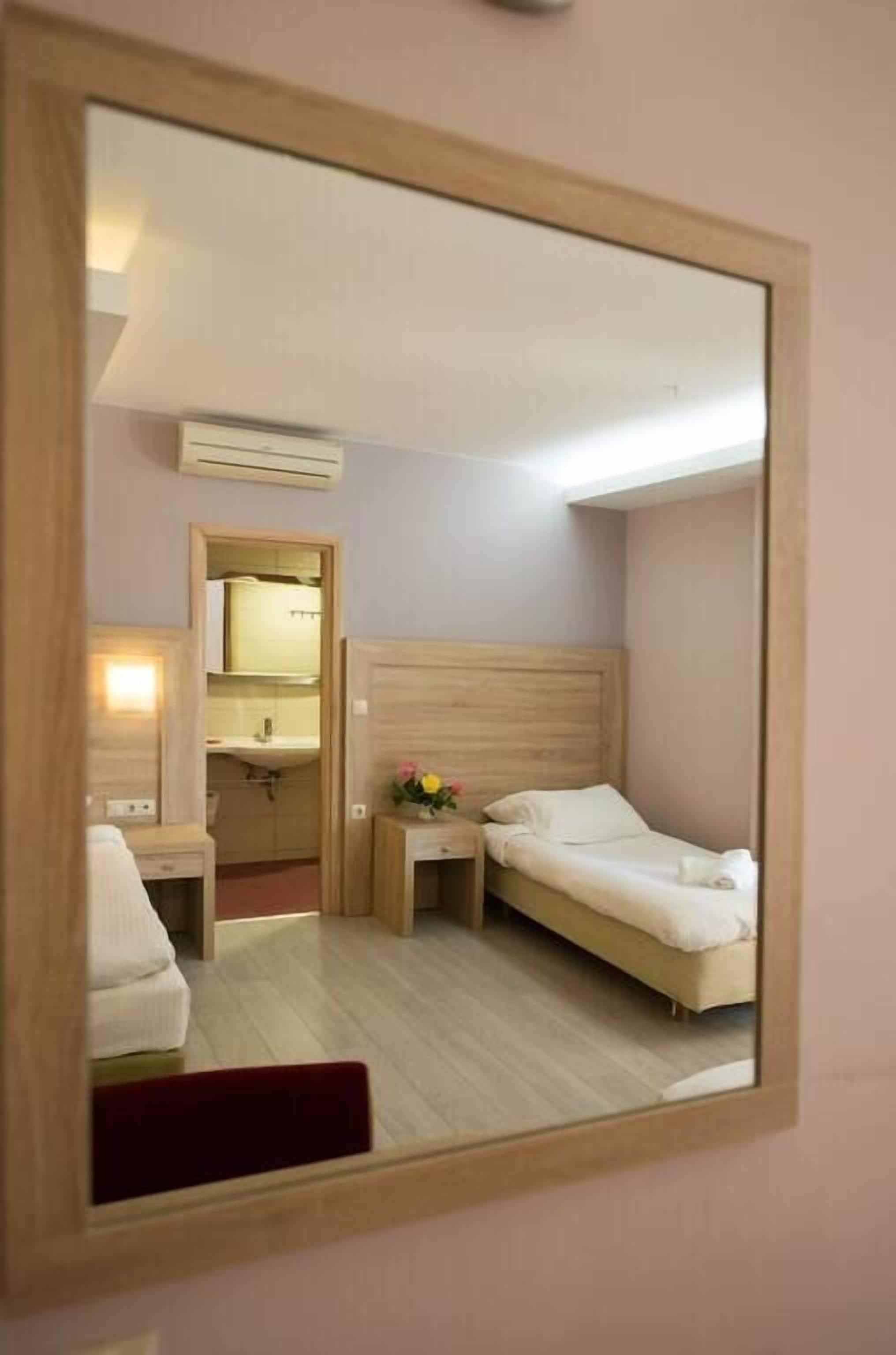 Habitación de hotel con una cama de cabecera de madera, una mesita de noche con un jarrón de flores, un espejo y un baño visible a través de una puerta abierta.