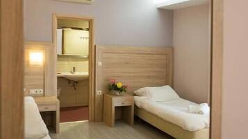 Habitación de hotel con una cama de cabecera de madera, una mesita de noche con un jarrón de flores, un espejo y un baño visible a través de una puerta abierta.
