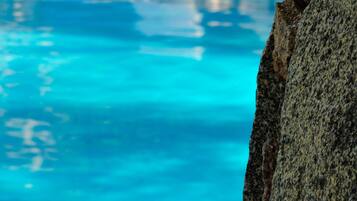 A swimming pool with lounge chairs and a stone wall.