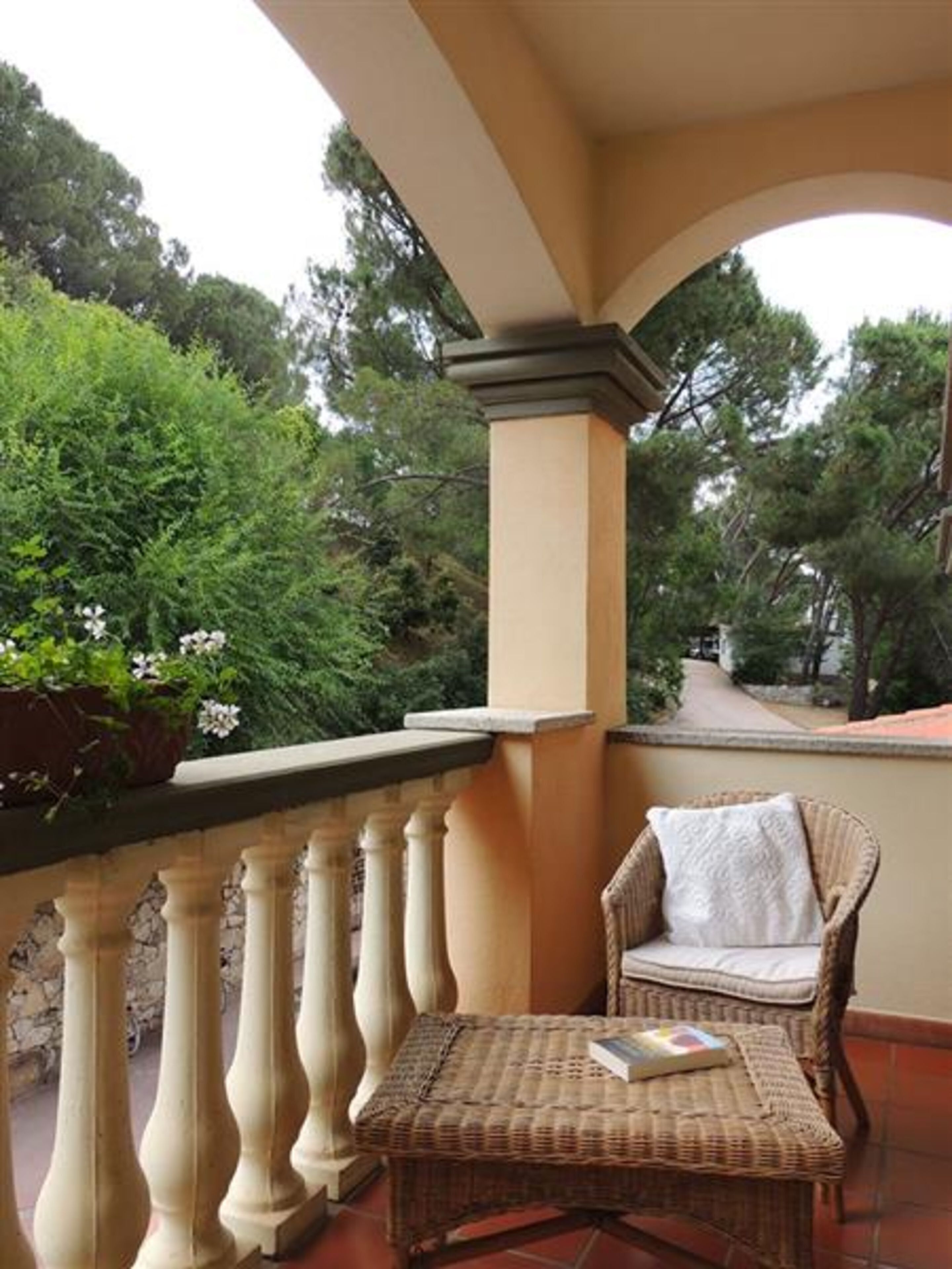 Un balcon agrémenté d’un fauteuil en osier et d’une table, entouré de verdure et doté d’un sol carrelé.