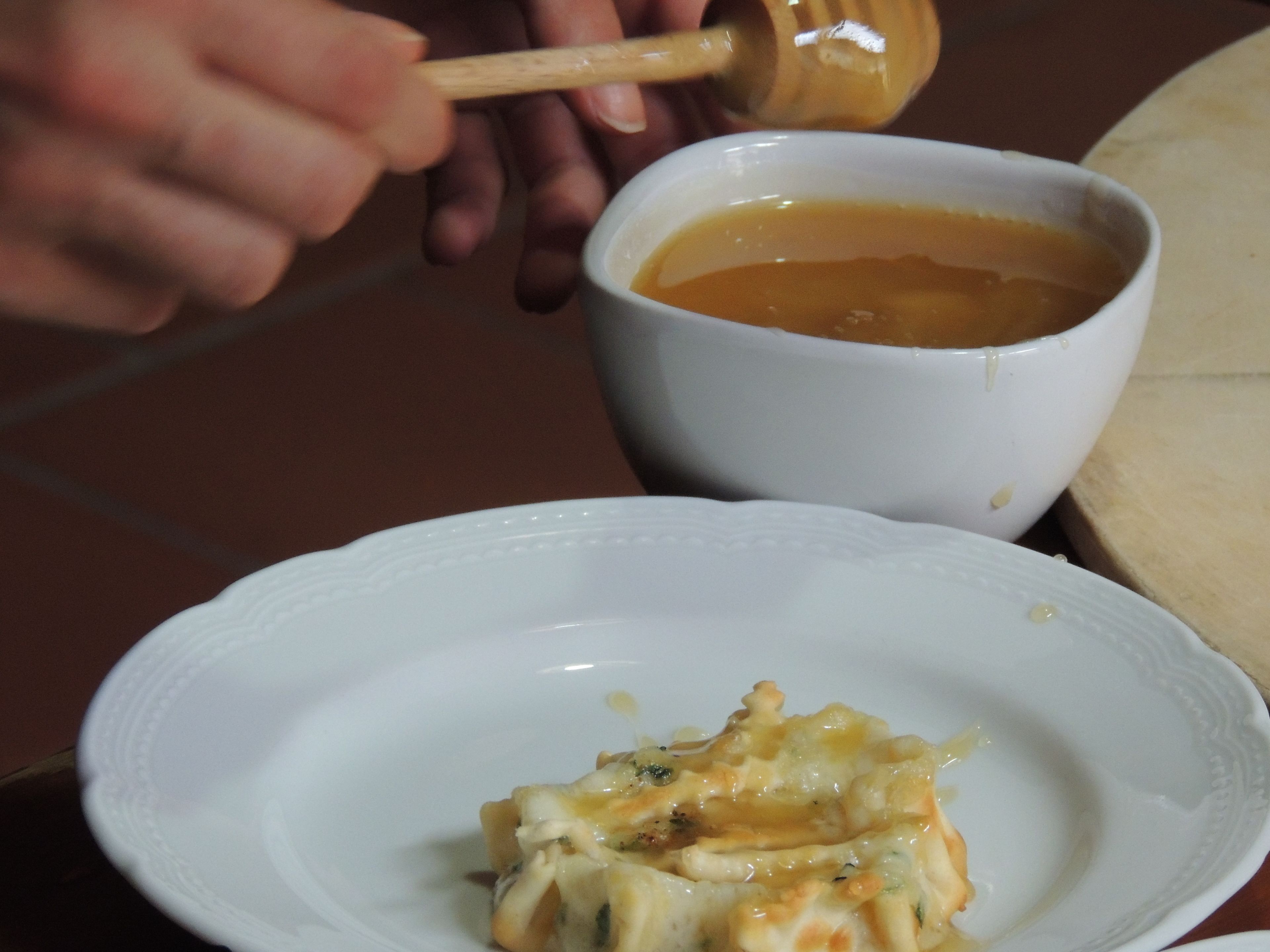 A white plate with a food item topped with melted cheese, a white bowl with a liquid, and a wooden spoon.