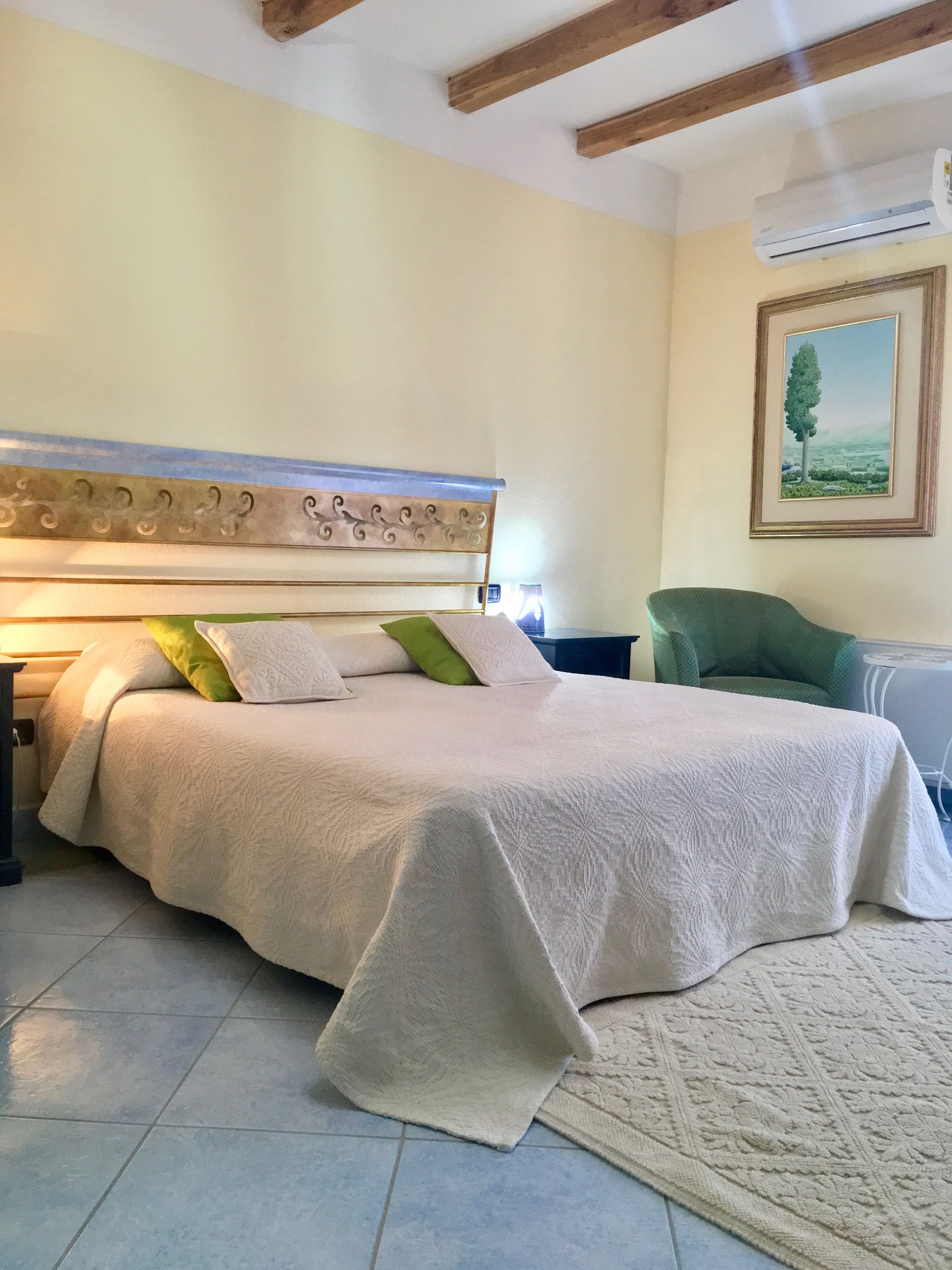 Een slaapkamer met een groot bed, een nachtkastje, een groene stoel, een ingelijst schilderij aan de muur en een plafondventilator.